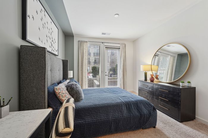 Elegant bedroom with a plush gray upholstered bed, chic decor, and abundant natural light from French doors.
