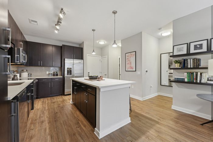 Modern kitchen with sleek dark cabinets, stainless steel appliances, expansive white island, elegant pendant lighting, and chic wood flooring.