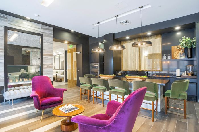 Luxurious modern living room with vibrant purple armchairs, sleek bar area with green stools, and cozy fireplace.