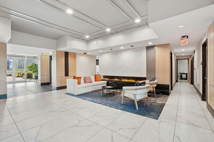 Elegant apartment lobby featuring a cozy seating area with modern furniture, accent pillows, and a sleek marble floor, enhanced by a stylish linear fireplace.