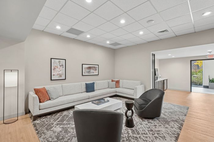 Sophisticated living room with modern lighting, plush gray sectional, stylish chairs, and chic artwork on neutral walls.