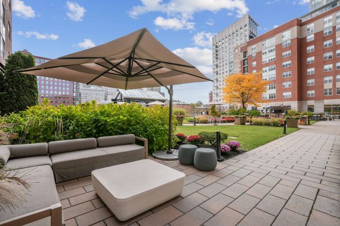 Chic apartment courtyard featuring a cozy patio with modern seating and umbrella, lush greenery, and a vibrant garden, perfect for relaxing and entertaining.