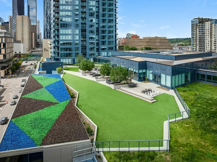 Vibrant urban space featuring a modern high-rise with lush green rooftop terrace, artistic landscaping, and stunning city views.