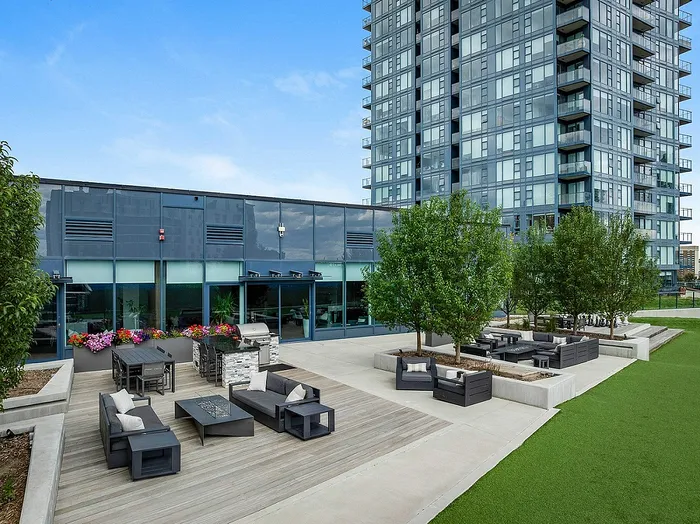 Aerial view of outdoor terrace with modern seating, vibrant flowers, and lush greenery against a backdrop of a contemporary high-rise building.