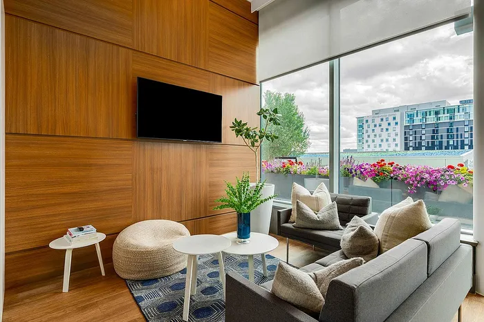 Modern living room with plush gray seating, vibrant floral balcony, and a wall-mounted TV against elegant wood paneling.