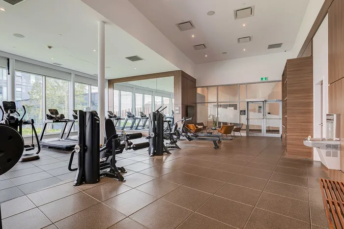 Modern gym with state-of-the-art equipment, large windows for natural light, and cozy seating area for relaxation.