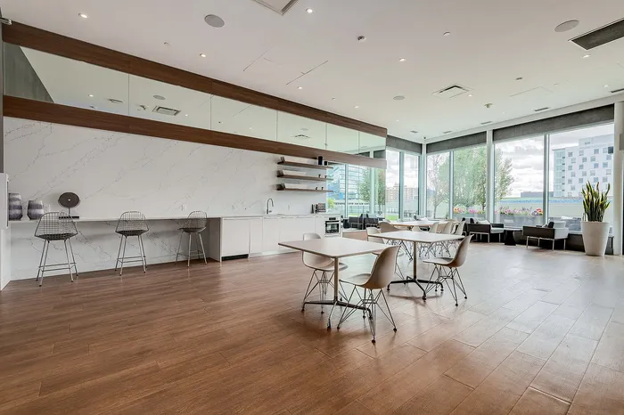 Modern communal lounge with sleek kitchen, chic seating, and large windows showcasing a vibrant cityscape view.