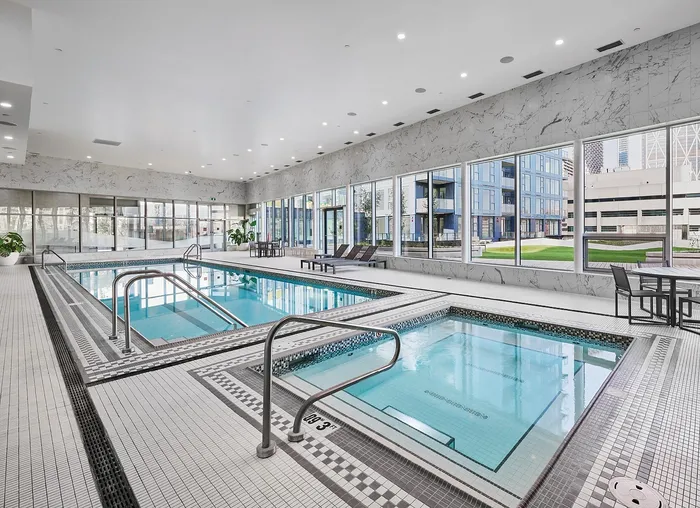 Luxurious indoor pool area with modern decor, abundant natural light, and city views through large windows.