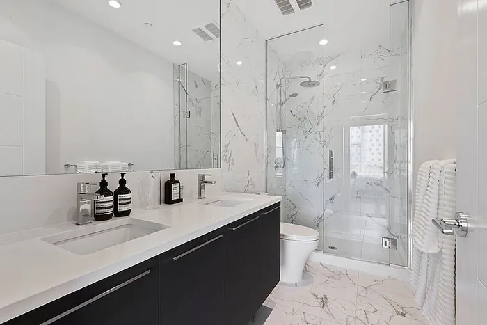 Luxurious bathroom featuring sleek white marble tiling, dual sinks, and a spacious glass-enclosed shower.
