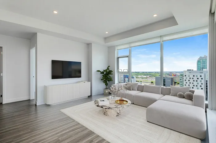 Bright, modern living room with sleek flooring, large windows boasting a city view, cozy sectional sofa, and stylish marble coffee table.
