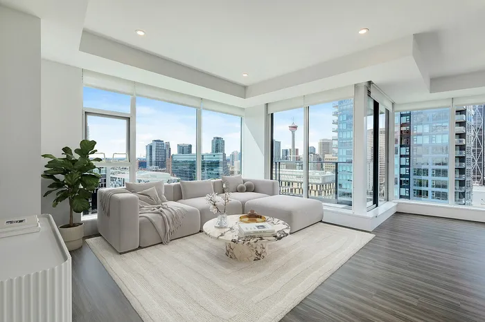 Modern living room with floor-to-ceiling windows offering breathtaking city skyline views, featuring a plush grey sectional sofa and stylish marble coffee table.