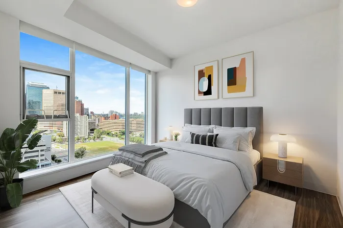 Luxurious bedroom with a stunning cityscape view, featuring a plush bed, modern decor, and ample natural light through floor-to-ceiling windows.