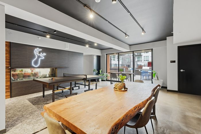 Modern recreational area featuring a sleek ping pong table, stylish wooden dining table, and vibrant decor with natural light streaming in through large windows.