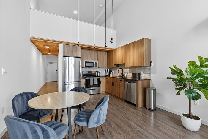 Modern kitchen with sleek wooden cabinets, stainless steel appliances, and a cozy dining area in a bright, stylish apartment.