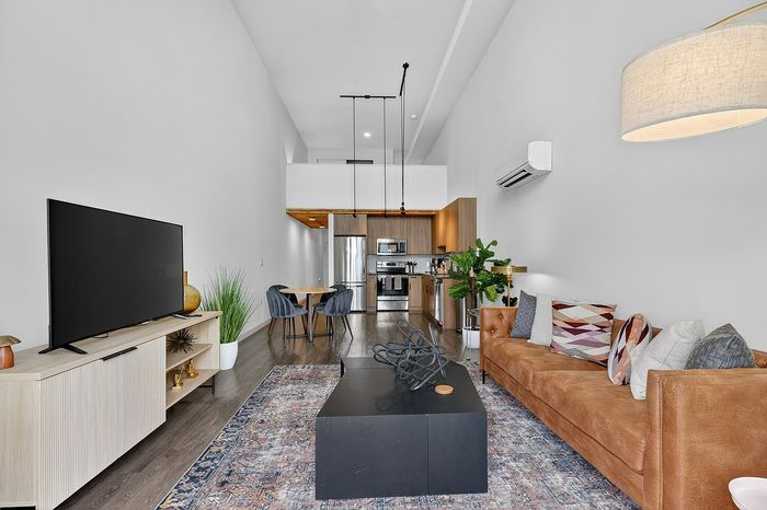 Open-plan living room with stylish decor, a cozy leather sofa, modern TV setup, and a sleek kitchen in the background.