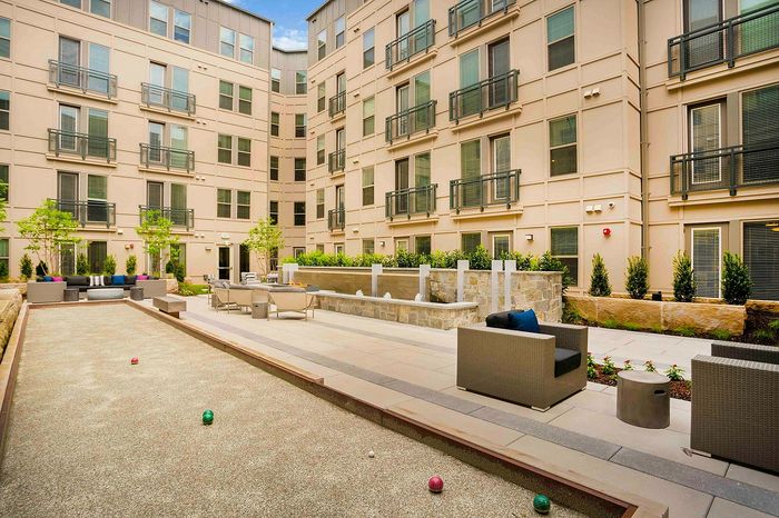 Chic apartment courtyard featuring modern seating, lush greenery, and a bocce ball court for leisure and relaxation.