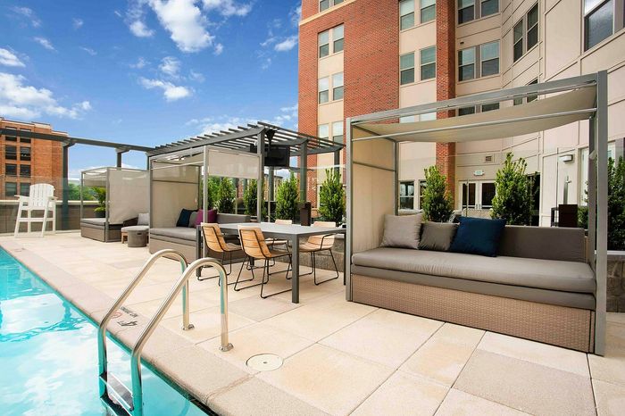 Luxurious apartment pool with modern lounge seating and stylish cabanas under a clear blue sky.