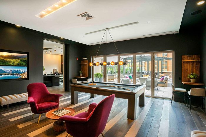 Luxurious apartment lounge room featuring a modern pool table, vibrant seating, and expansive windows opening to a stylish outdoor lounge area.