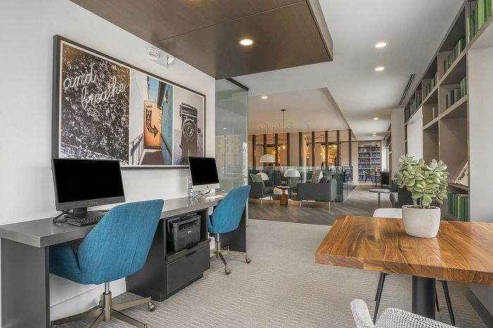 Sophisticated workspace with modern decor, featuring sleek computers, vibrant blue chairs, and a cozy lounge area in a stylish open-concept design.