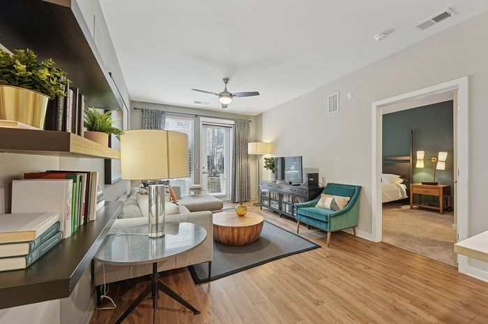 Modern living room featuring elegant wood flooring, cozy seating, and abundant natural light, opening into a stylish bedroom. Perfect for contemporary apartment living.