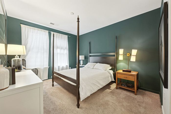 Elegant bedroom with rich green walls, four-poster bed, and bright natural light creating a cozy and serene atmosphere.