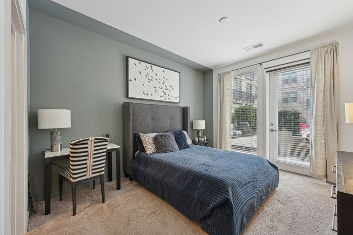 Modern bedroom with a plush grey headboard, elegant desk, and large windows inviting natural light and garden views.