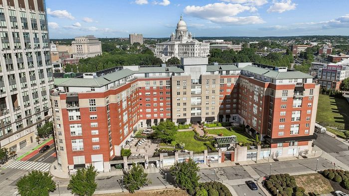 Aerial view of a vibrant, modern apartment complex with lush green gardens and a scenic city backdrop, highlighting urban charm and convenience.
