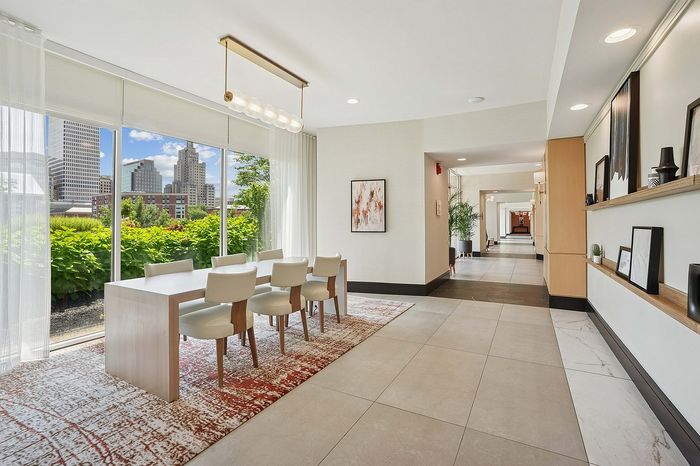 Elegant lounge area with a modern table and chairs, featuring large windows offering a stunning cityscape view and abundant natural light.