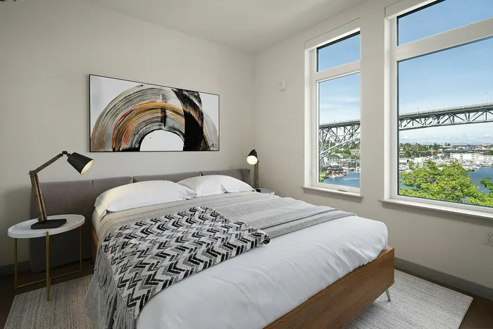 Bright and cozy bedroom with modern decor, stunning waterfront view from large windows, and stylish abstract art on the wall.
