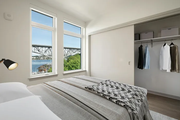 Elegant bedroom with a cozy bed, open wardrobe, and stunning waterfront view through large windows.
