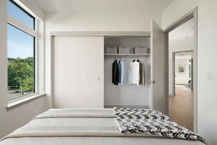 Bright and airy bedroom with a large window showcasing a scenic view, stylish closet space with organization, and a cozy ambient feel.