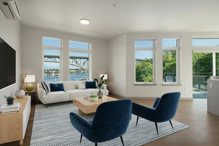 Elegant living room with stunning water and bridge views, featuring large windows, modern decor, and a cozy seating area with plush blue chairs.