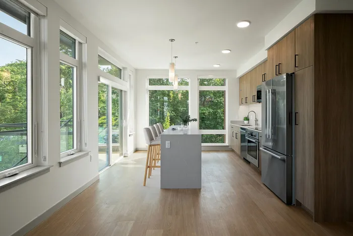 Modern kitchen with elegant island, sleek appliances, and large windows offering lush green views.