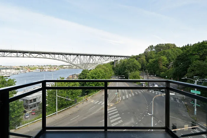 Breathtaking view of a serene river and iconic bridge from a modern balcony, surrounded by lush greenery and lively cityscape.
