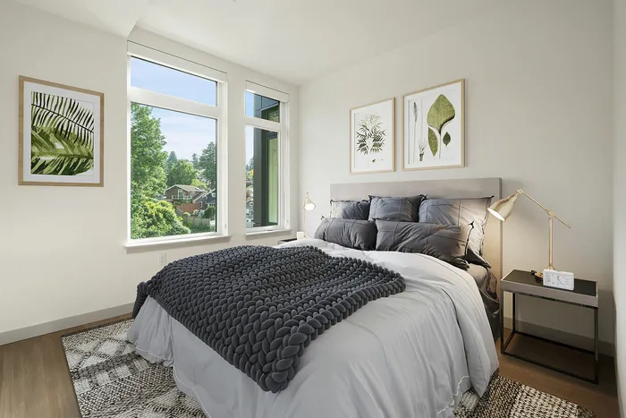 Bright and inviting bedroom featuring large windows with green views, cozy gray bedding, and elegant decor.