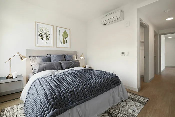 Elegant bedroom with modern decor, featuring a cozy bed with a plush knitted blanket, stylish bedside lamp, and nature-themed artwork on the wall.
