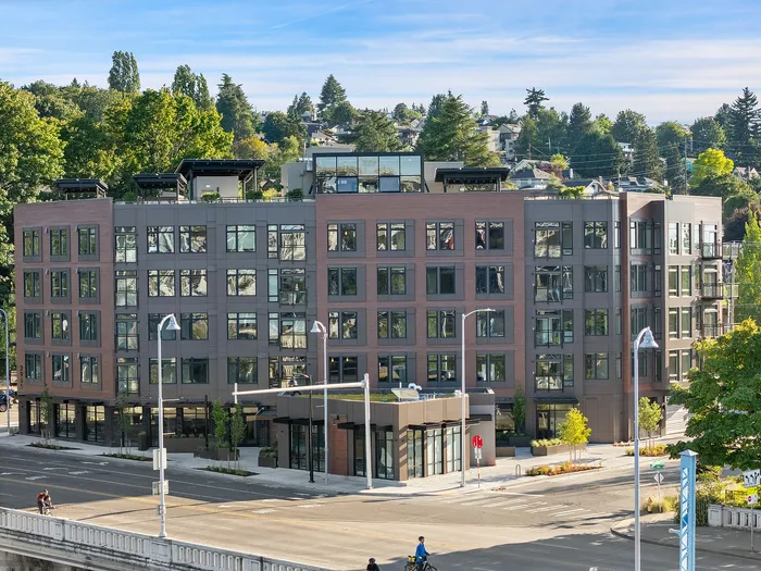 Modern five-story apartment building with expansive windows and lush rooftop terraces, surrounded by greenery and cityscape views.