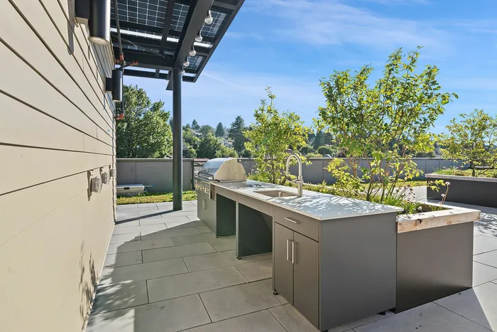 Chic outdoor kitchen with sleek countertops, built-in grill, and lush greenery under a sunlit sky, perfect for entertaining.