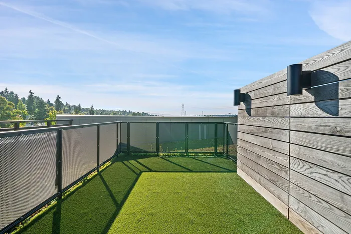 Sunlit rooftop terrace with lush green artificial turf, modern railing, and scenic views of trees and sky.