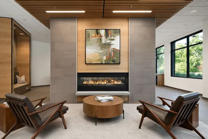 Modern lounge area featuring sleek wooden accents, a cozy fireplace, abstract art, and large windows with lush views.