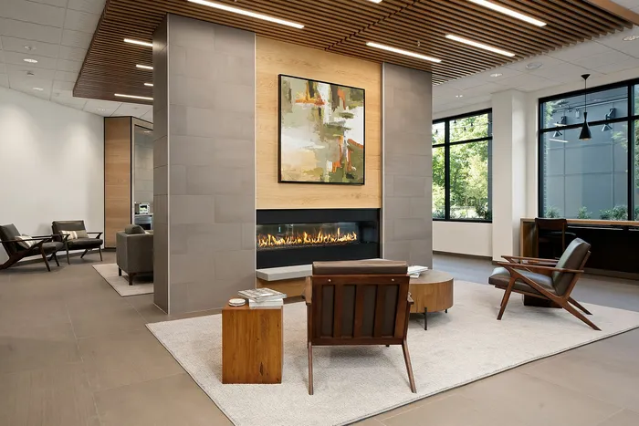 Elegant modern lobby with a cozy fireplace, stylish wooden furniture, and artistic decor, offering a welcoming atmosphere and ample natural light from large windows.