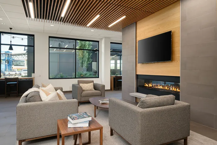 Modern living room with cozy gray sofas, a sleek fireplace, mounted TV, and natural light streaming through large windows, featuring elegant wood and tile accents.