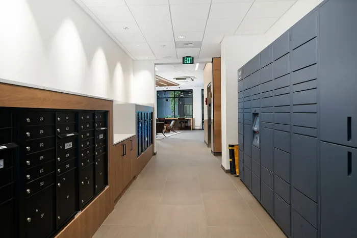 Modern apartment hallway featuring sleek mail slots and secure package lockers, leading to a chic lounge area.