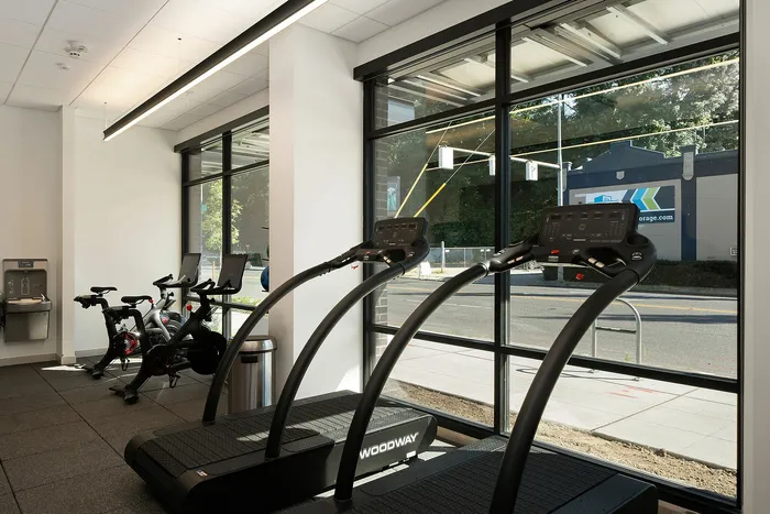 Modern fitness center with large windows featuring state-of-the-art treadmills and stationary bikes, offering an inviting workout ambiance.