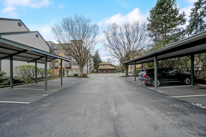 Inviting apartment complex exterior with ample covered parking, lush greenery, and a welcoming leasing office, perfect for comfortable living.