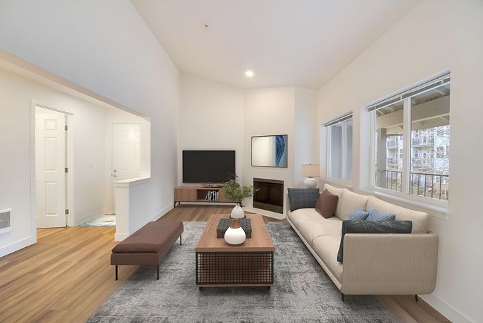 Bright and inviting living room boasting high ceilings, a cozy fireplace, and chic modern furnishings with large windows for natural light.