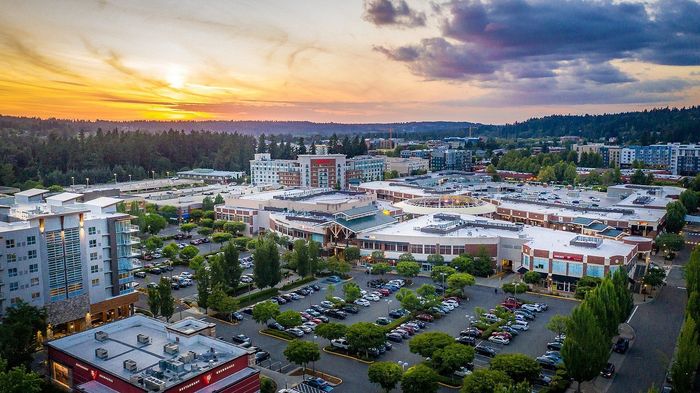 Vibrant aerial view of a bustling city center surrounded by nature, showcasing modern architecture and a stunning sunset.