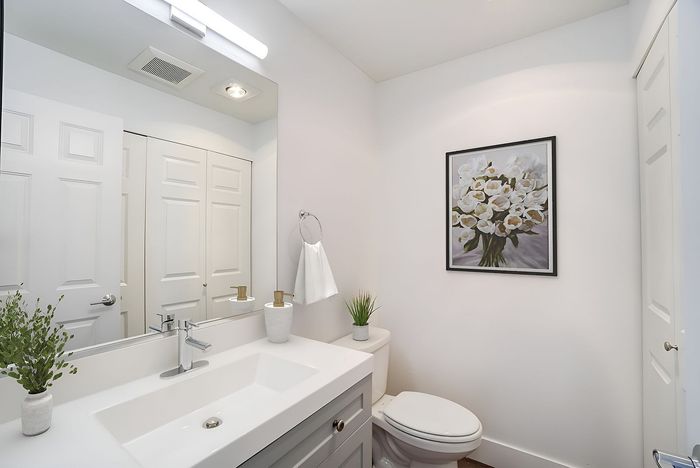 Bright and modern bathroom with elegant white fixtures, large mirror, and chic floral art. Cozy and stylish with green accents.
