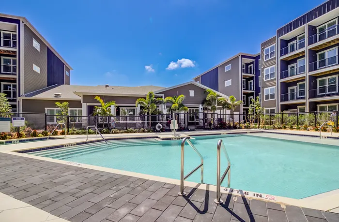 A large pool with crystal blue water next to a hot tub, clubhouse, and brand new apartments.