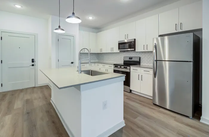 Unfurnished apartment kitchen with island seating, stainless steel appliances, white cabinets, and wood-style plank flooring at Garrett Forum in Fort Myers, Florida.